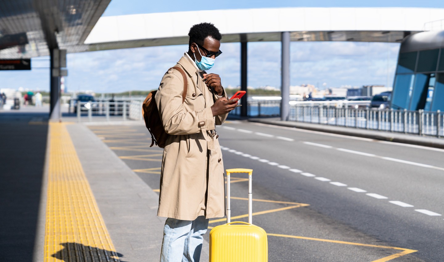  a man on his phone waiting with a suitcase outside an airport