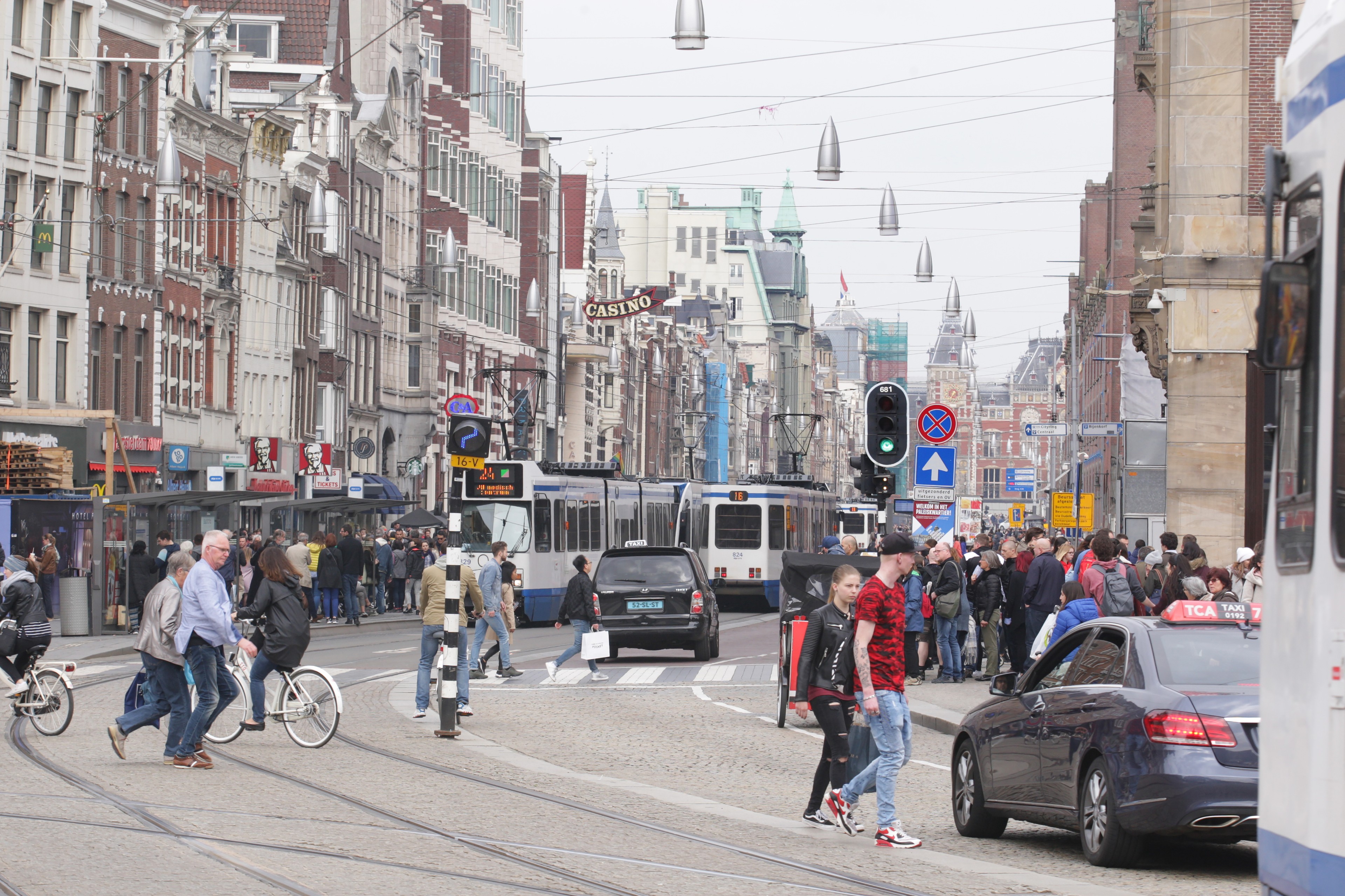 An image of an Amsterdam street showing cars, taxis, trams, pedestrians and cyclists.